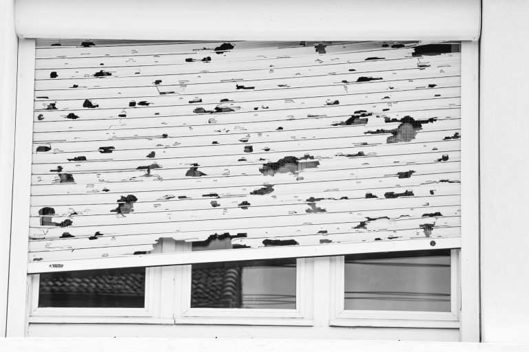 White window blinds with holes, shutters after the hailstorm, depicting hail damage